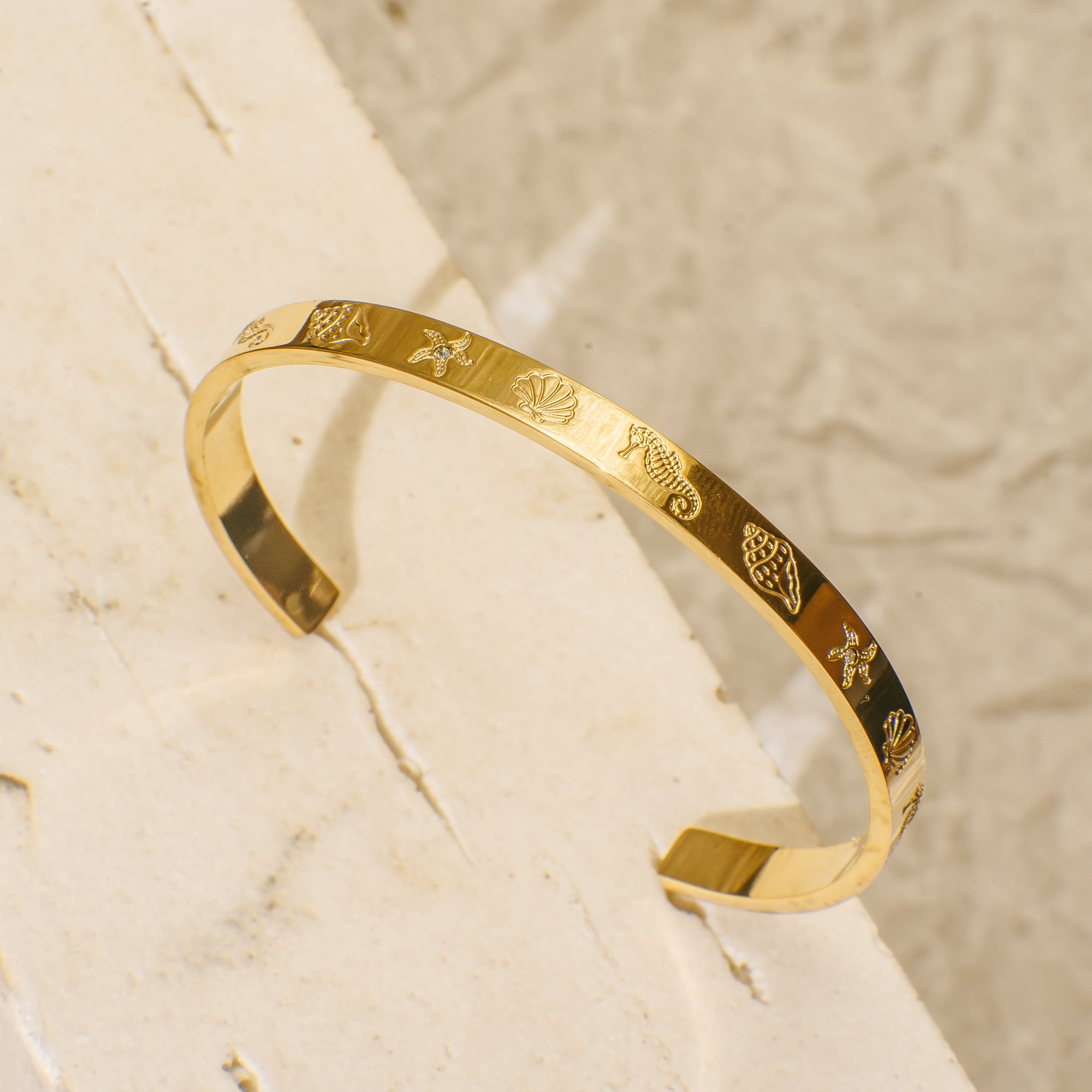 Gold bangle bracelet engraved with ocean-themed designs including seahorse, seashell, conch shell, and starfish
