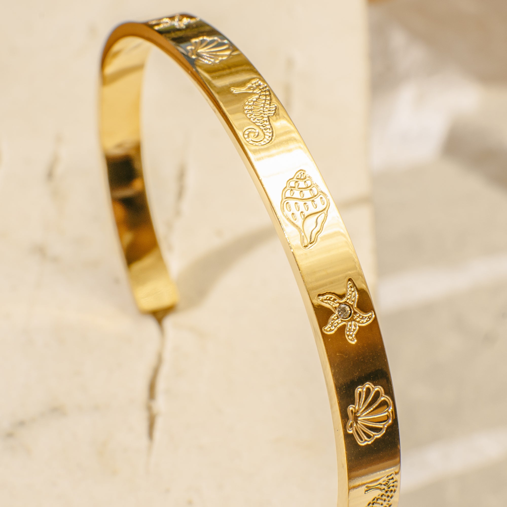 Gold bangle bracelet engraved with ocean-themed designs including seahorse, seashell, conch shell, and starfish