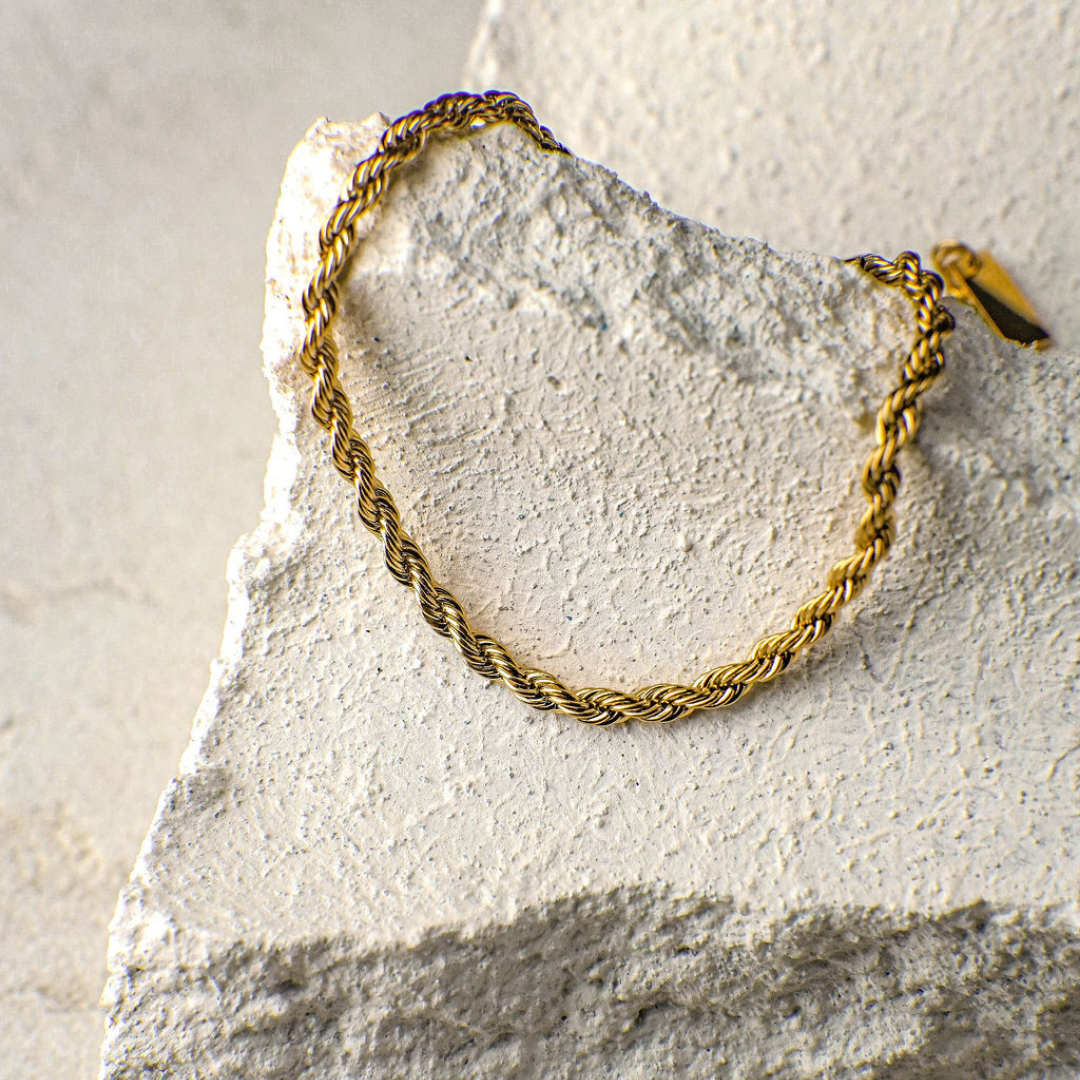 Gold braided bracelet on a textured stone surface