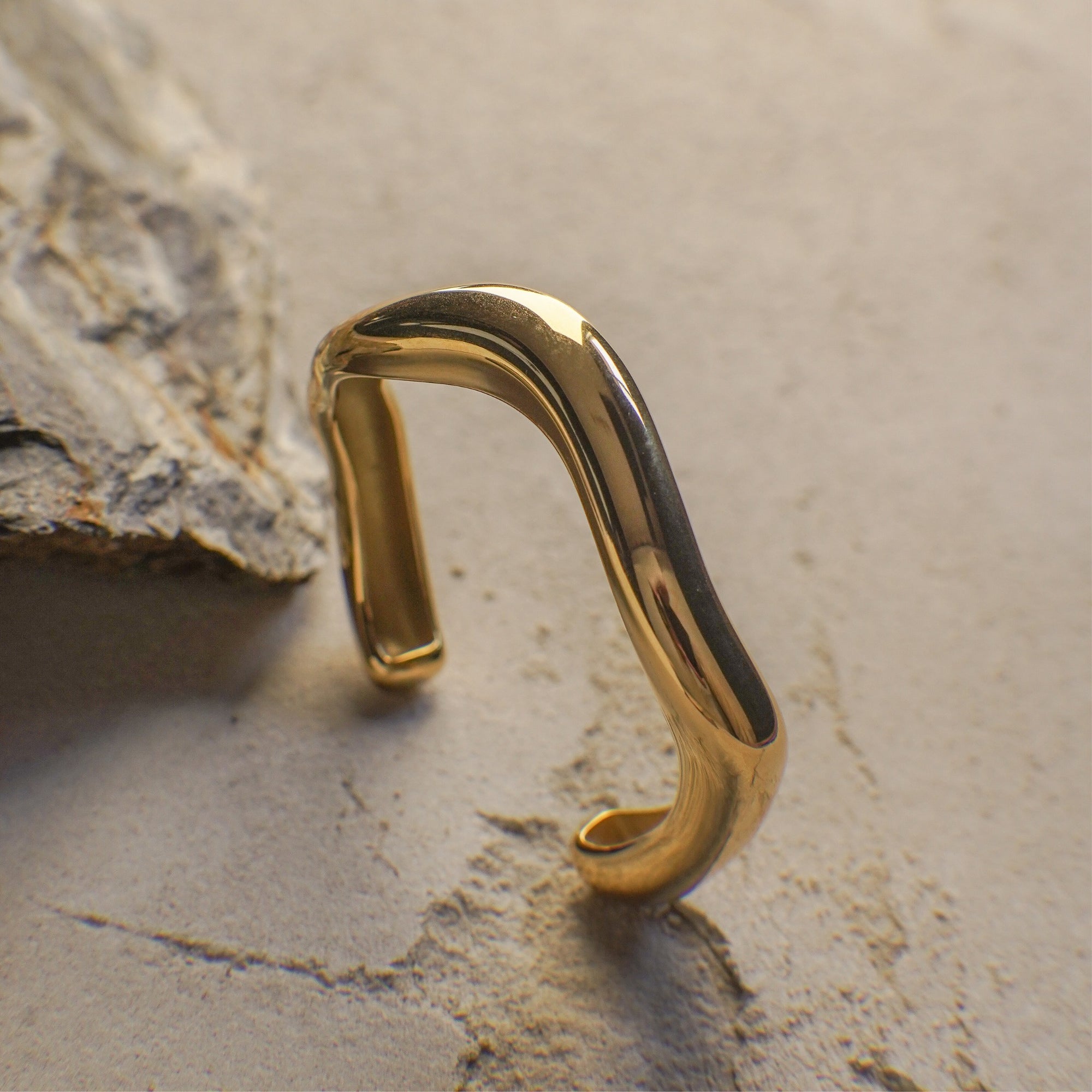 Gold curvy bangle on a textured stone surface
