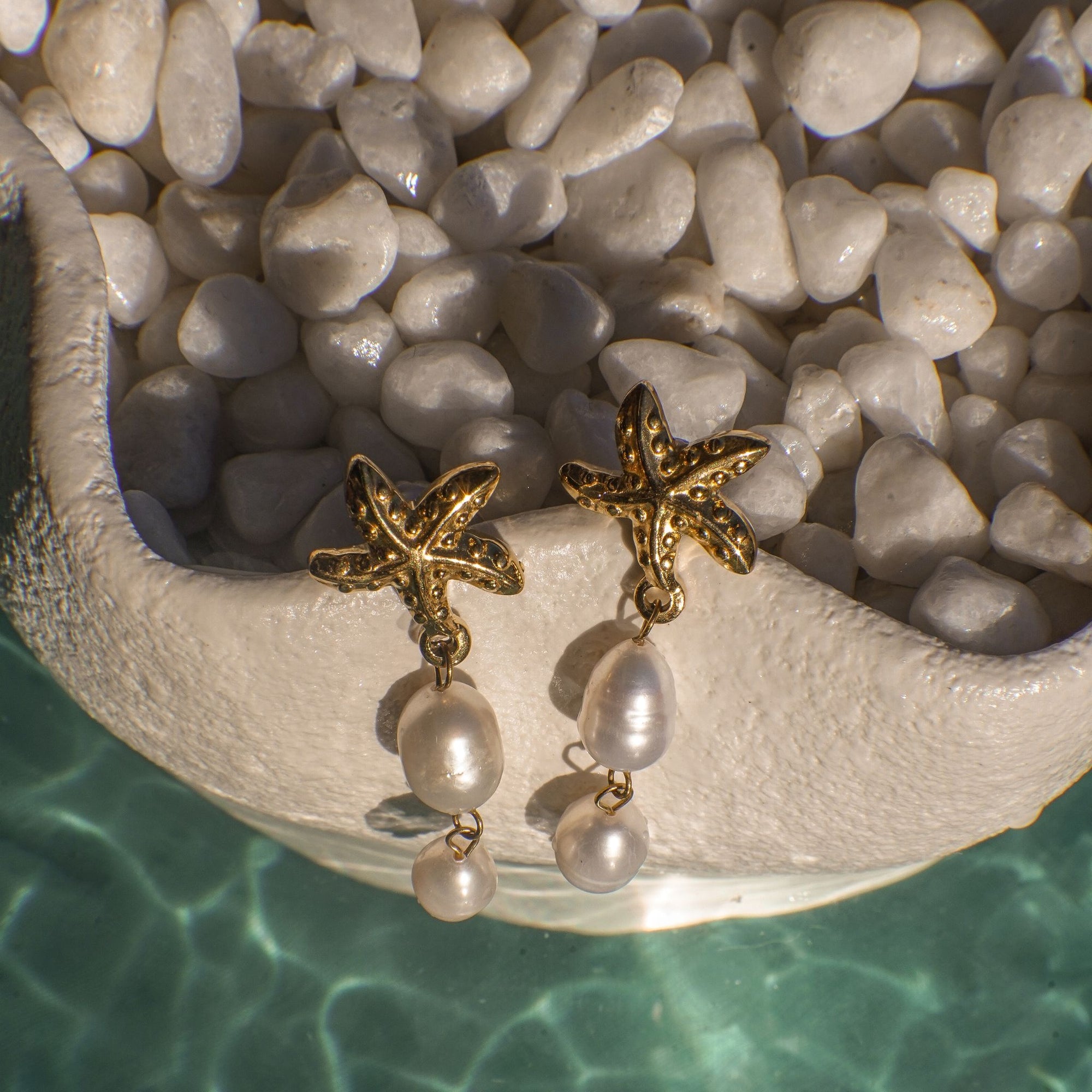 Gold starfish earrings with pearl drops on a stone surface