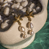 Gold starfish earrings with pearl drops on a stone surface near water.