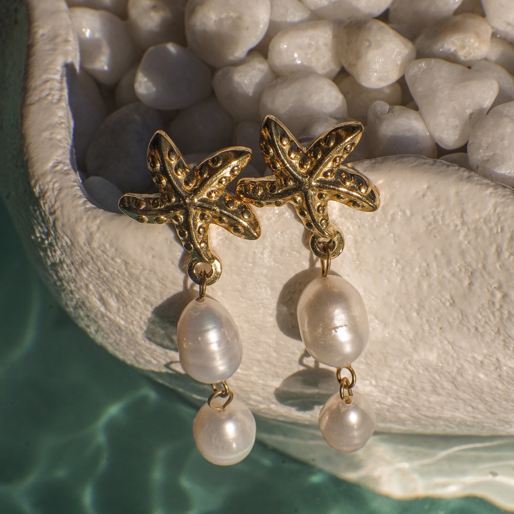 Gold starfish earrings with pearl drops on a stone surface