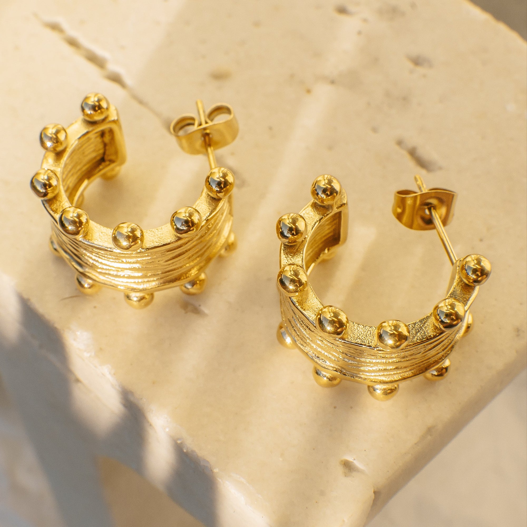 Gold hoop earrings with decorative elements on a beige surface