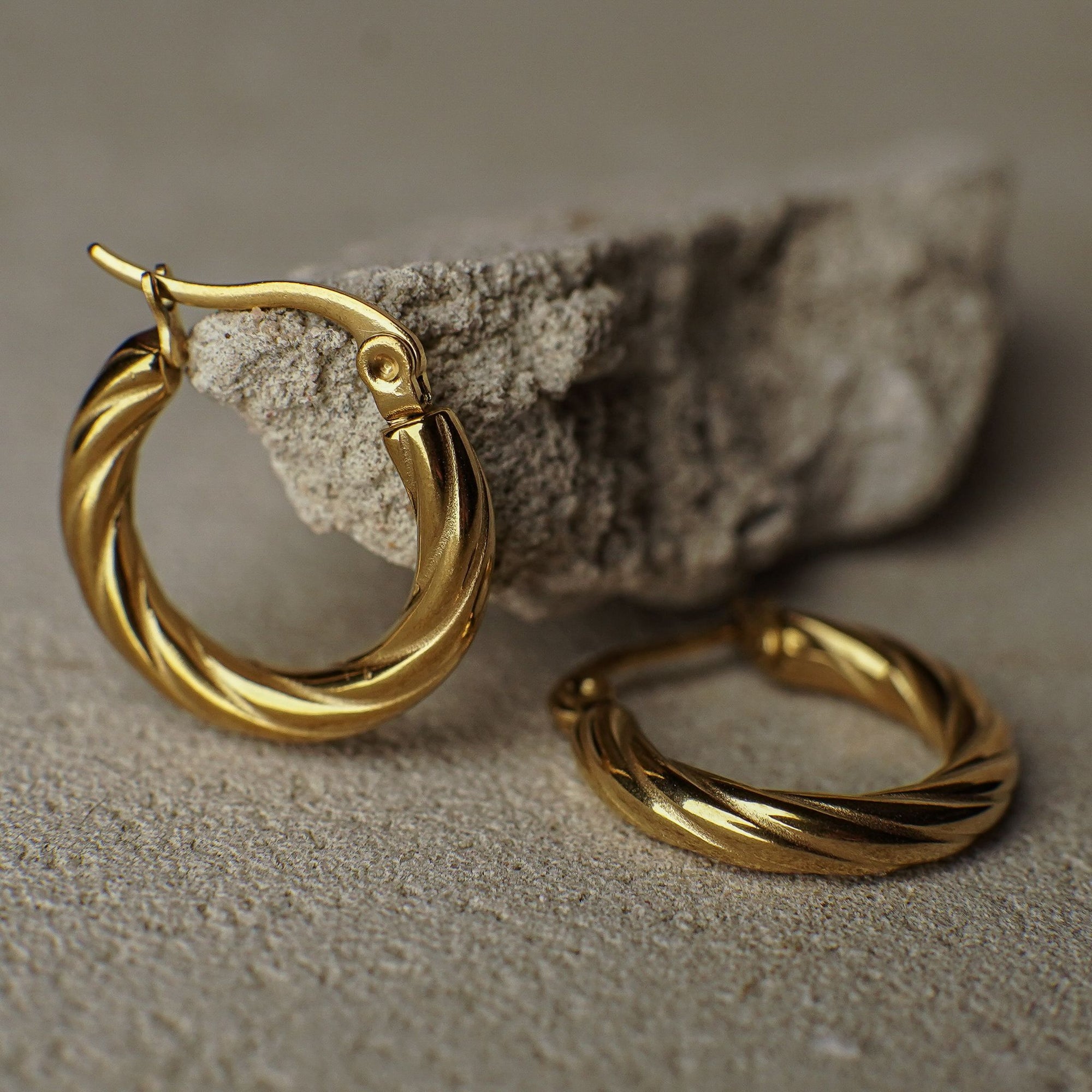 Gold hoop earrings on a textured surface with a neutral background