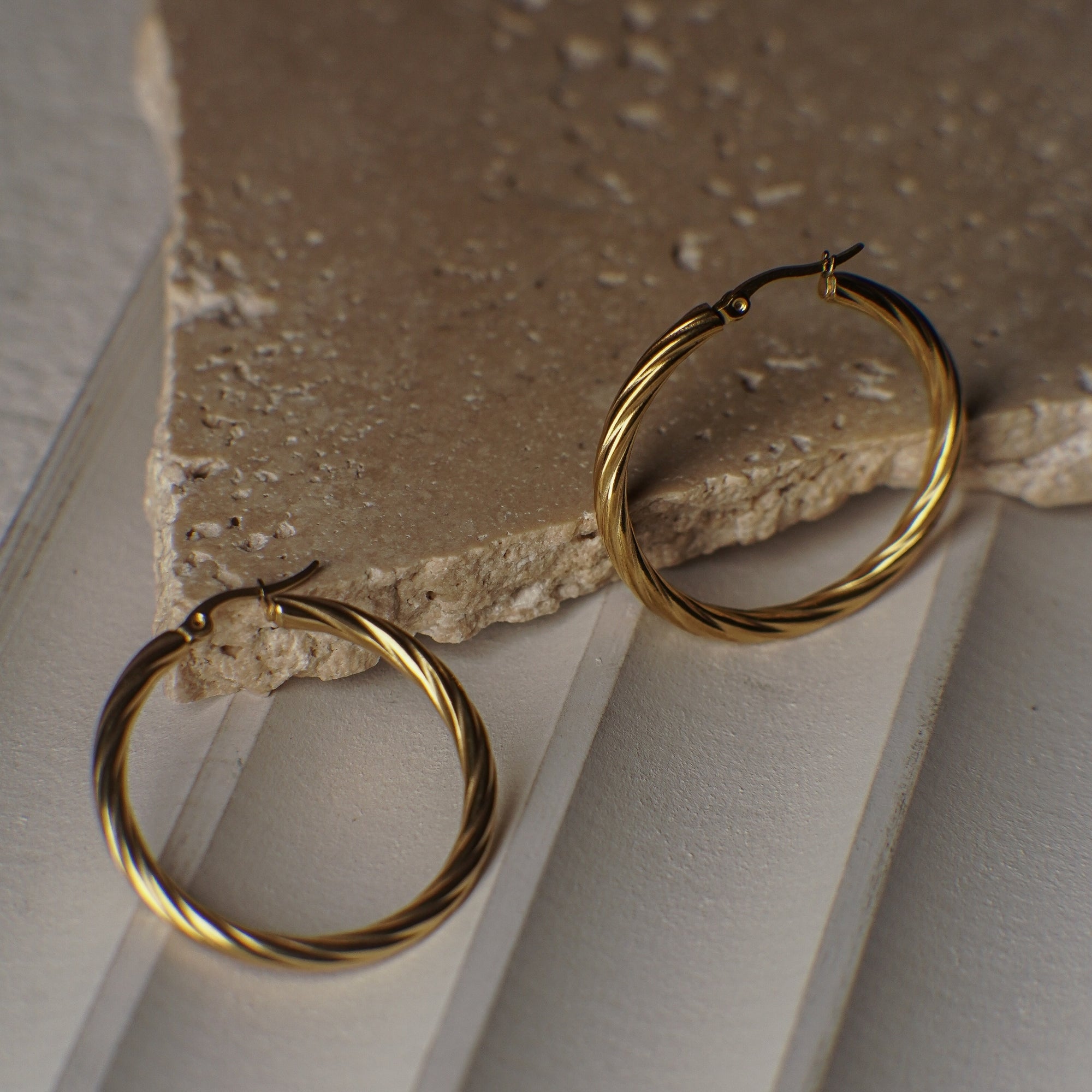 Gold hoop earrings on a stone surface