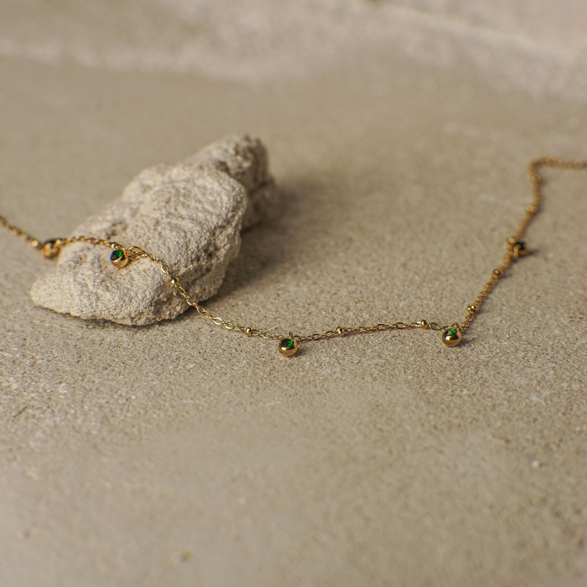 Gold necklace with green gemstones on a sandy surface