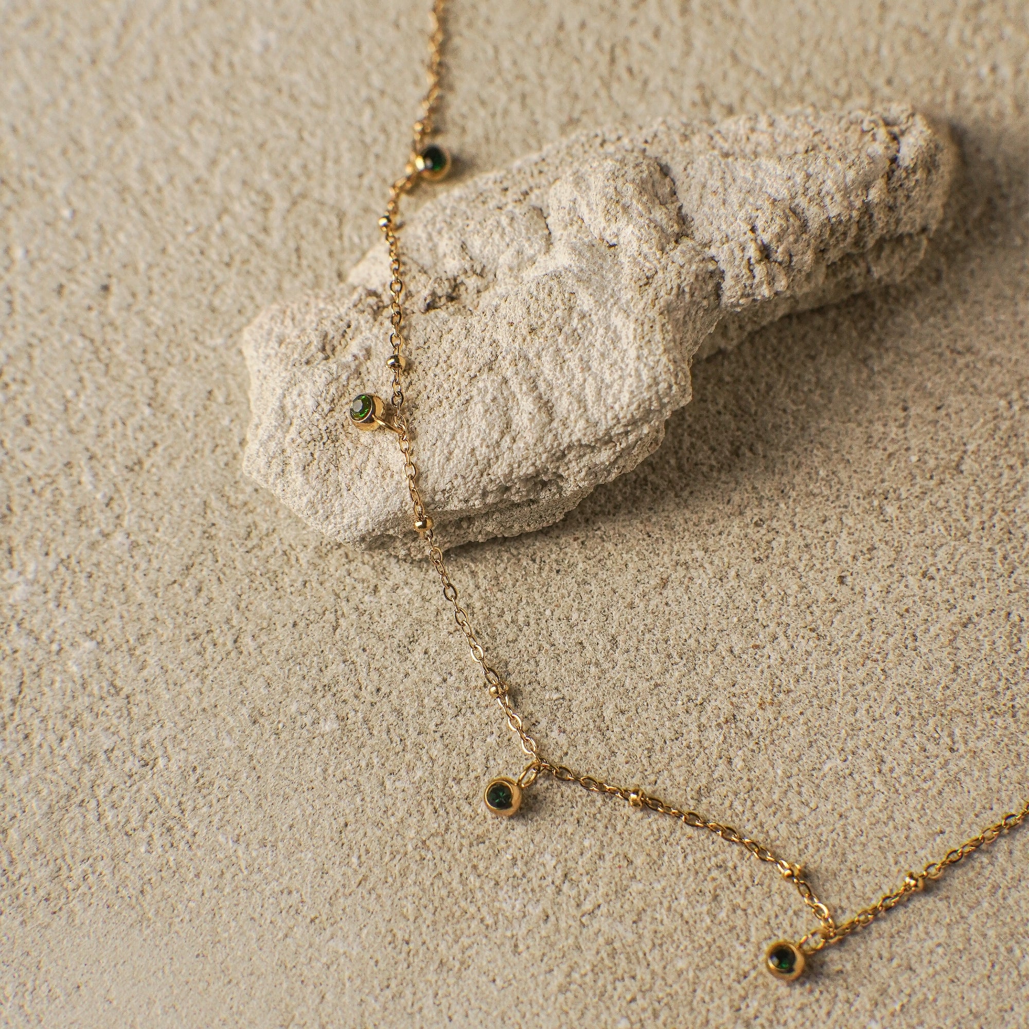 Gold necklace with green gemstones on a sandy surface