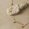 Gold necklace with green gemstones on a sandy surface