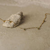 Gold necklace with green gemstones on a sandy surface