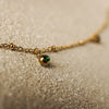 Gold bracelet with a green gemstone on a sandy surface