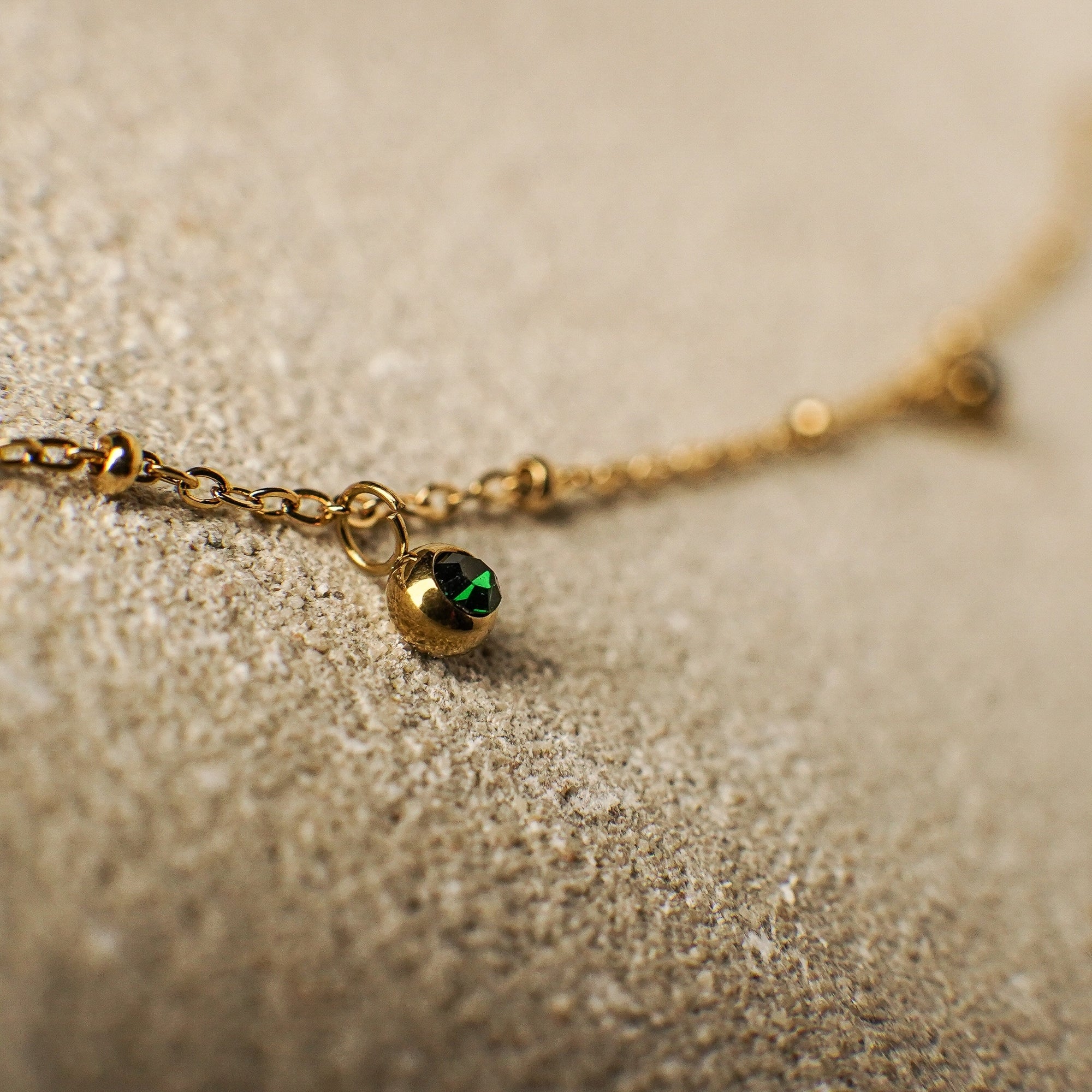 Gold bracelet with a green gemstone on a sandy surface