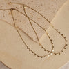 A gold-colored necklace with small, regular intervals of pearls displayed on a beige stone surface.