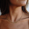 A gold-colored necklace with small, regular intervals of pearls displayed on a beige stone surface.