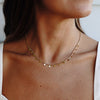 A gold-colored necklace with small, regular intervals of pearls displayed on a beige stone surface.