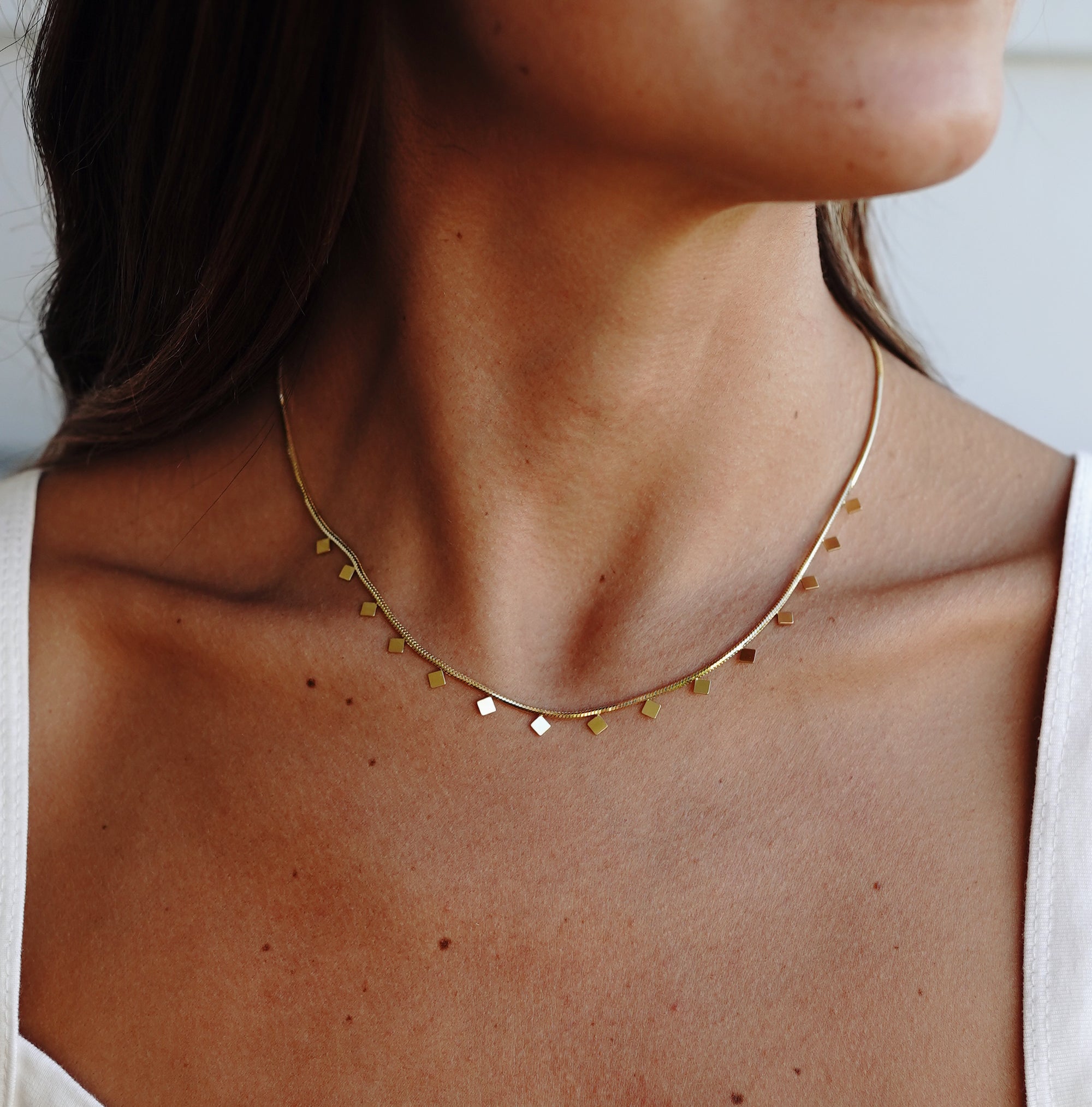 A gold-colored necklace with small, regular intervals of pearls displayed on a beige stone surface.