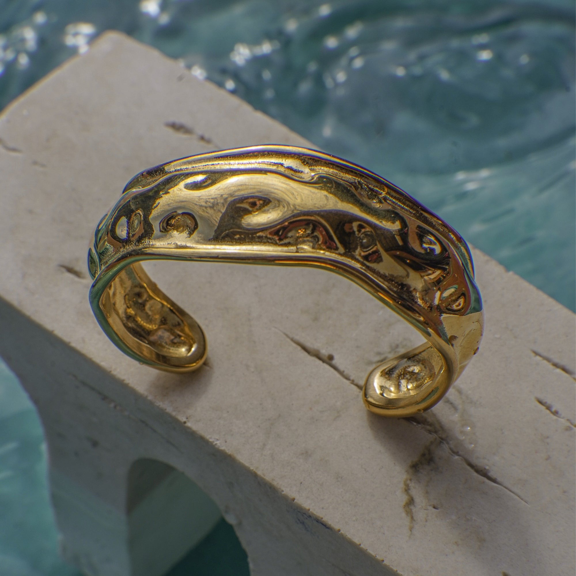 Gold bracelet on a stone ledge with water in the background