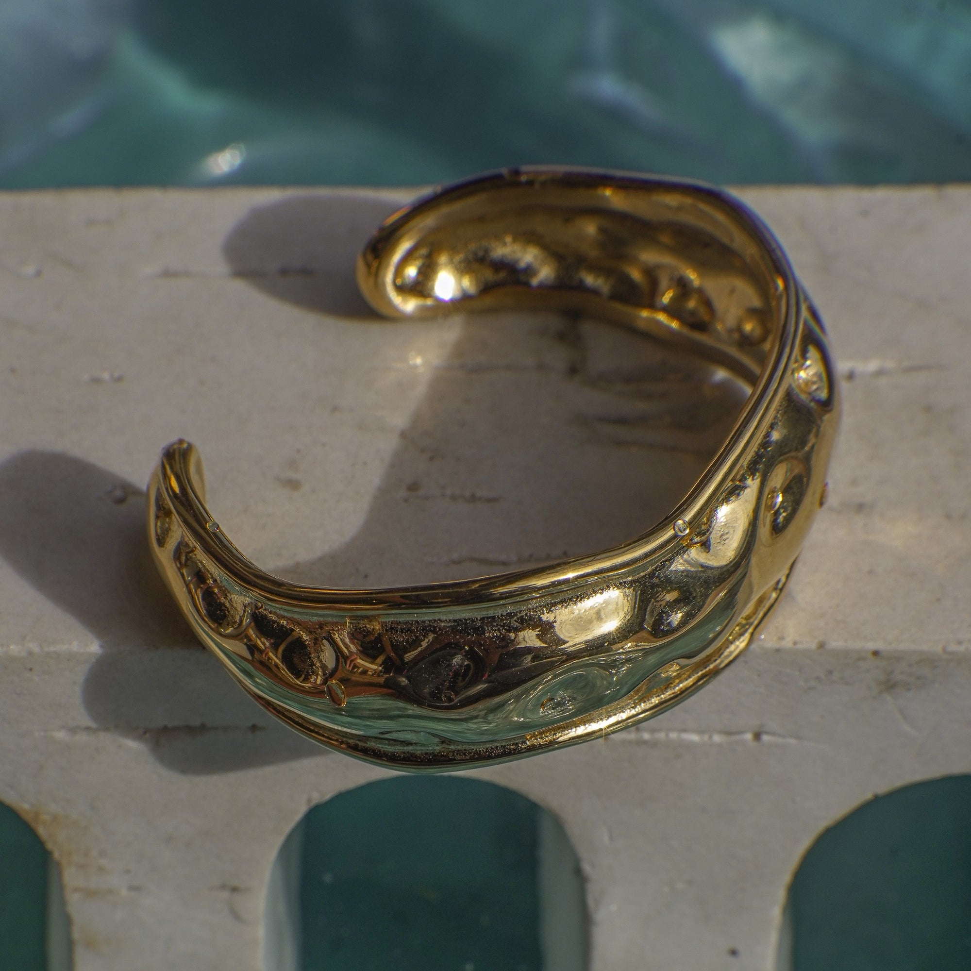Gold bracelet on a stone surface with a pool in the background