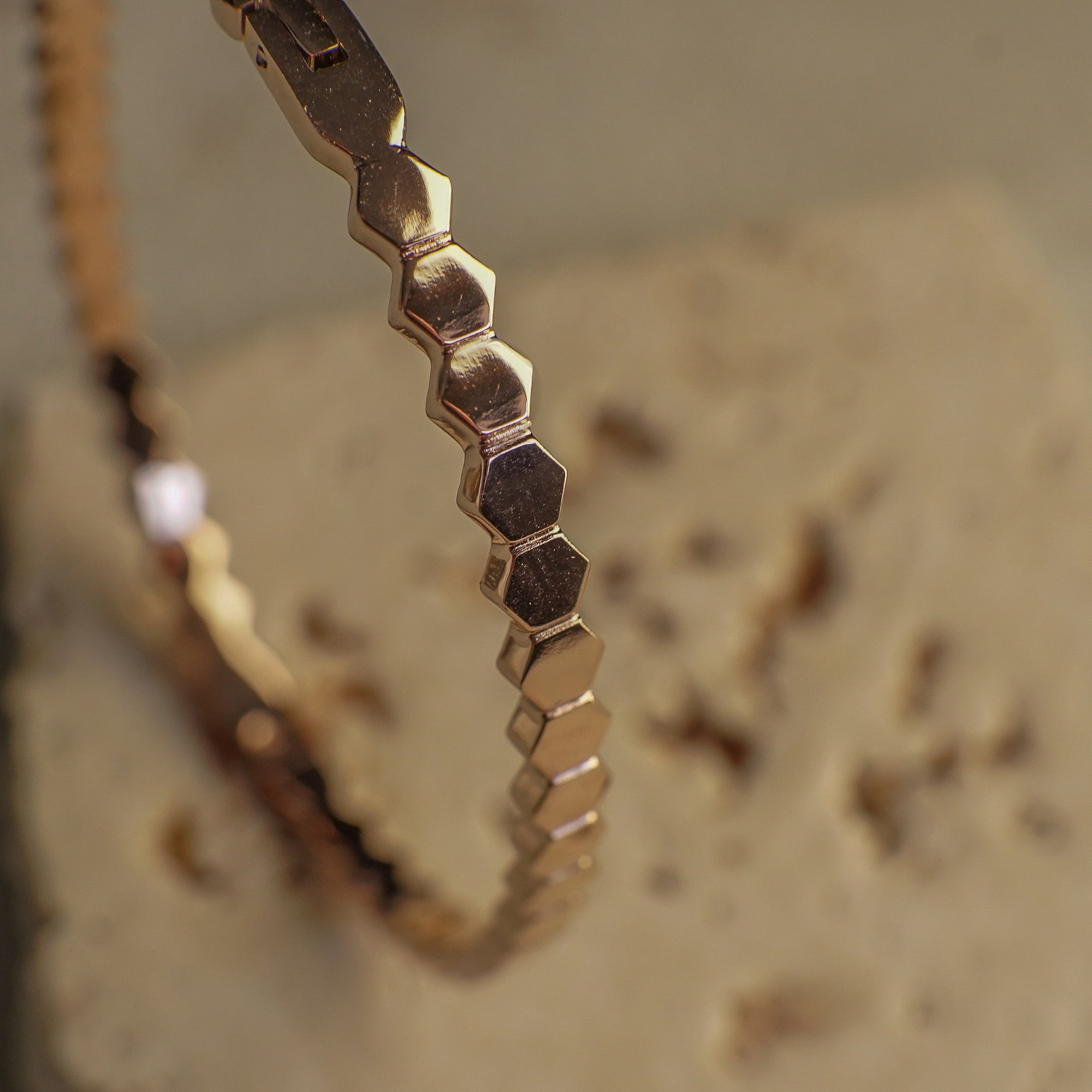 Gold bracelet with hexagonal pattern on a textured surface