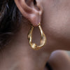 A woman wearing Nina Gold Drop Earrings on her right ear