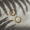 A pair of gold-colored hoop earrings on a textured background with a shadow cast over them.