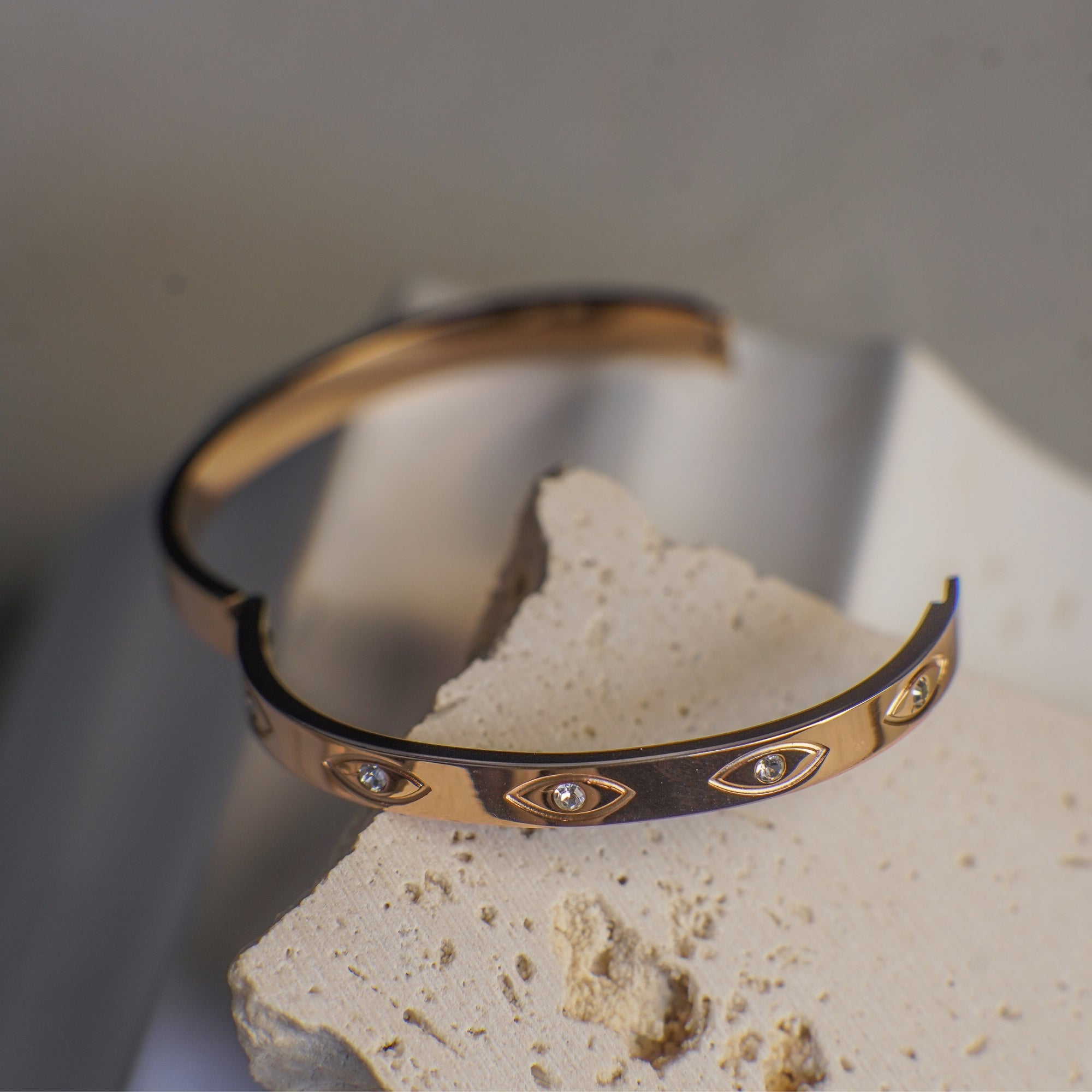 Gold and black bracelet with eye designs on a stone surface