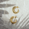 A pair of gold-colored hoop earrings on a crumpled silver paper background.