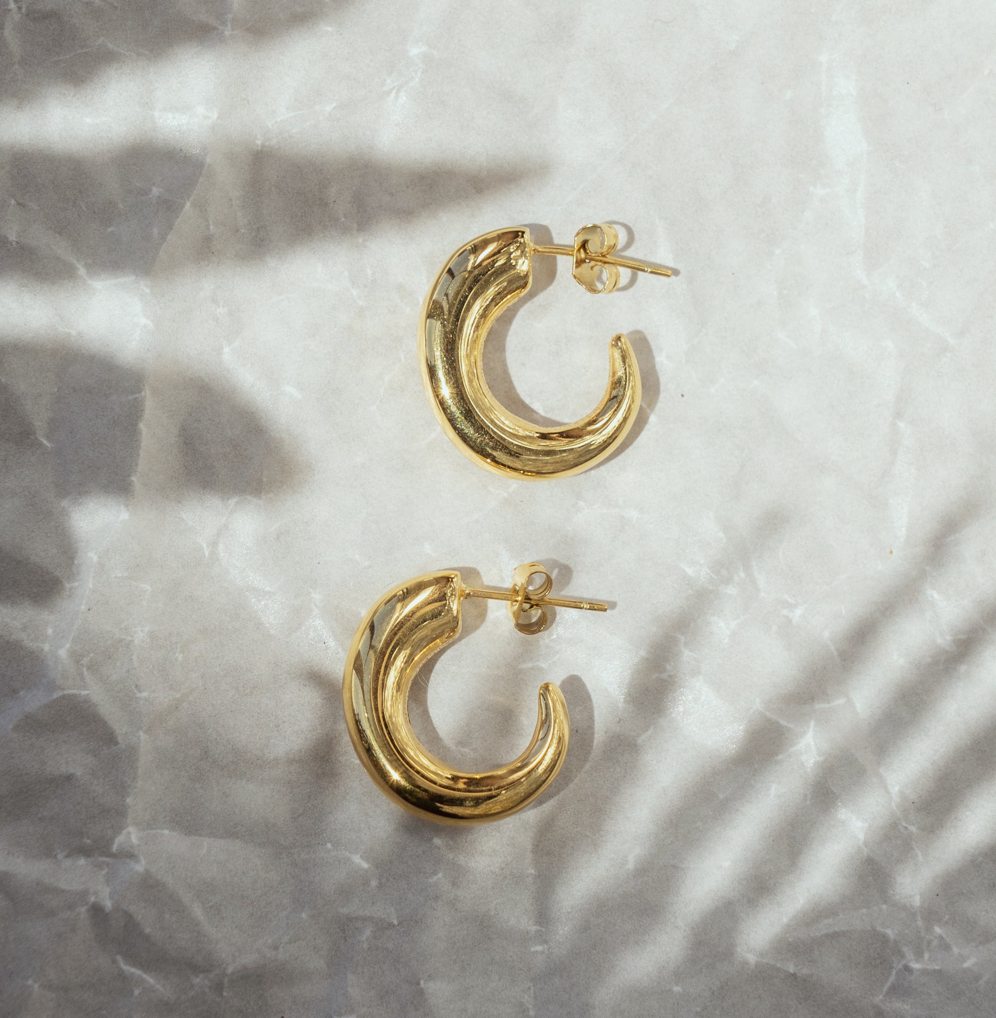 A pair of gold-colored hoop earrings on a crumpled silver paper background.