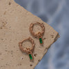 A pair of rose gold earrings with Emerald drop pendants on a textured surface.