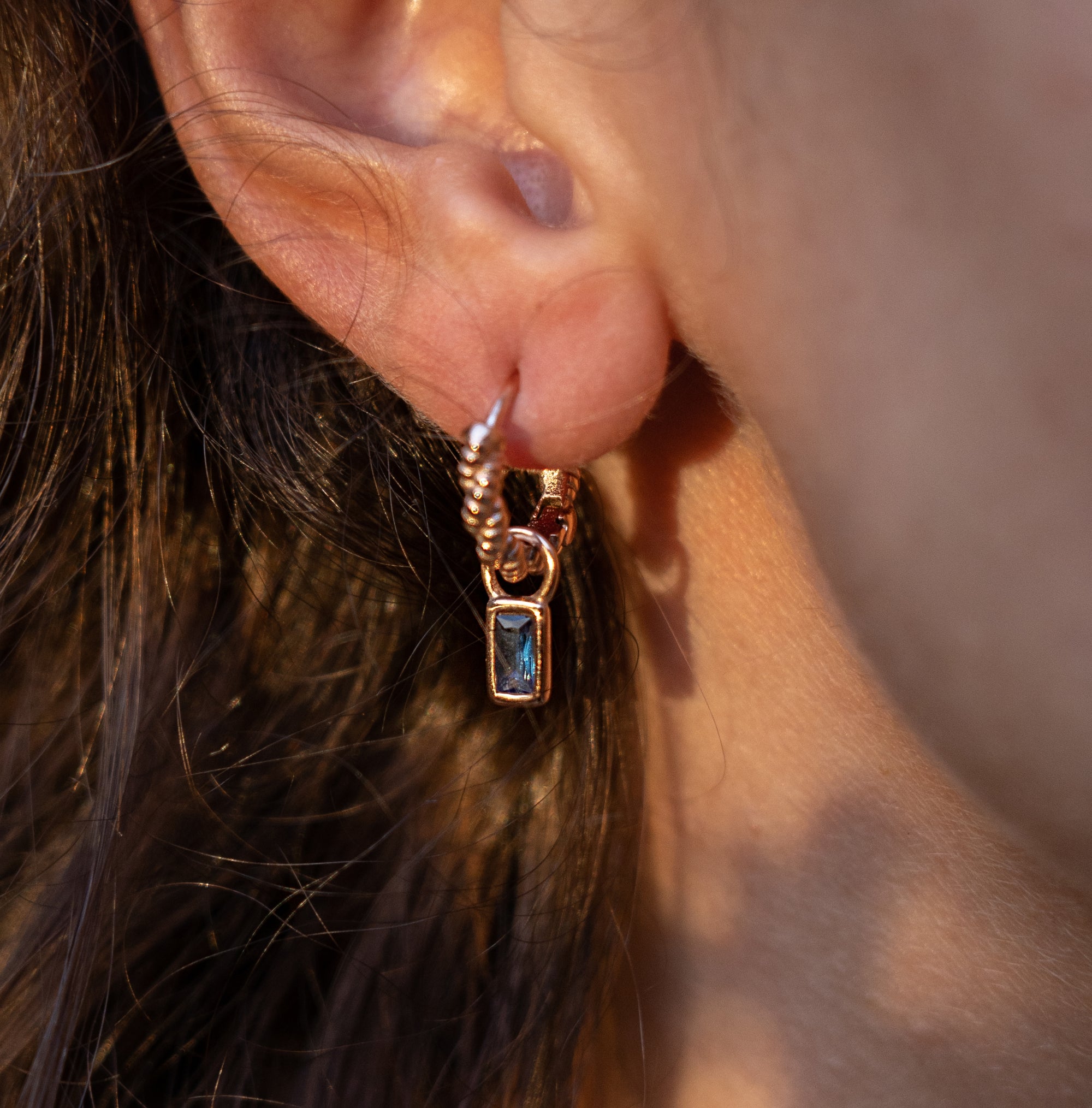 A rose gold earrings with a sapphire drop on a model's ear