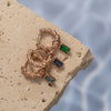 A collection of rose gold Zirconia stud earrings displayed on a light-colored surface with water droplets in the background.