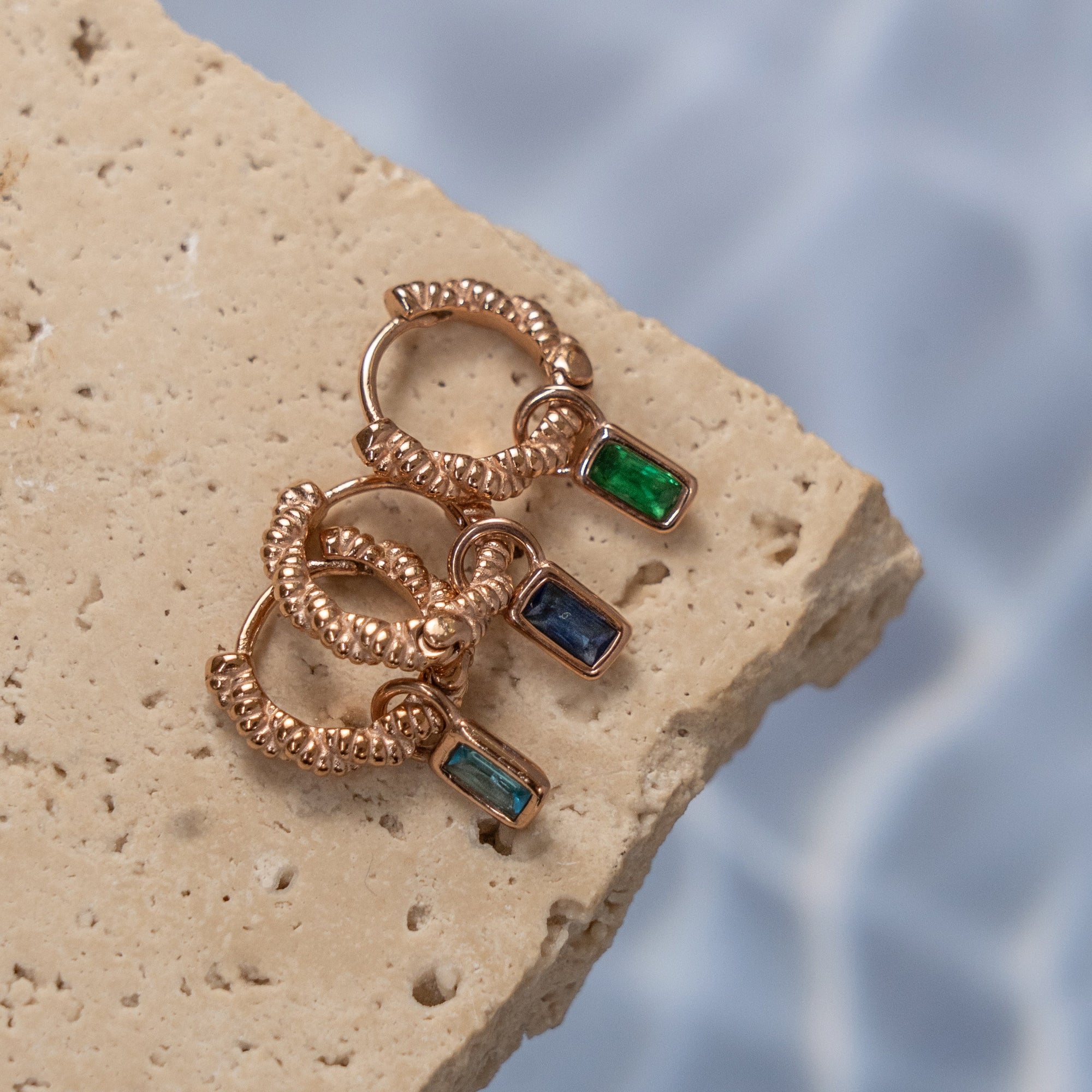 A collection of rose gold Zirconia stud earrings displayed on a light-colored surface with water droplets in the background.