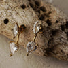 Gold earrings with clear gemstones on a textured stone surface