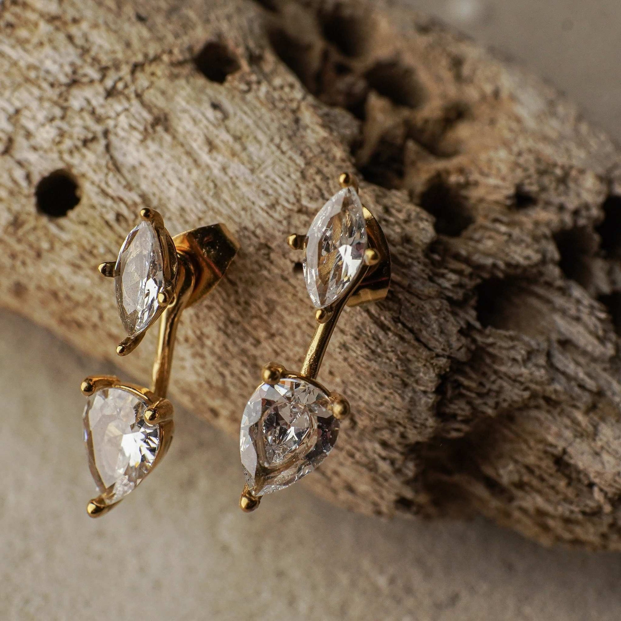 Gold earrings with clear gemstones on a textured stone surface