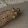 Gold earrings with clear stones on a piece of driftwood.