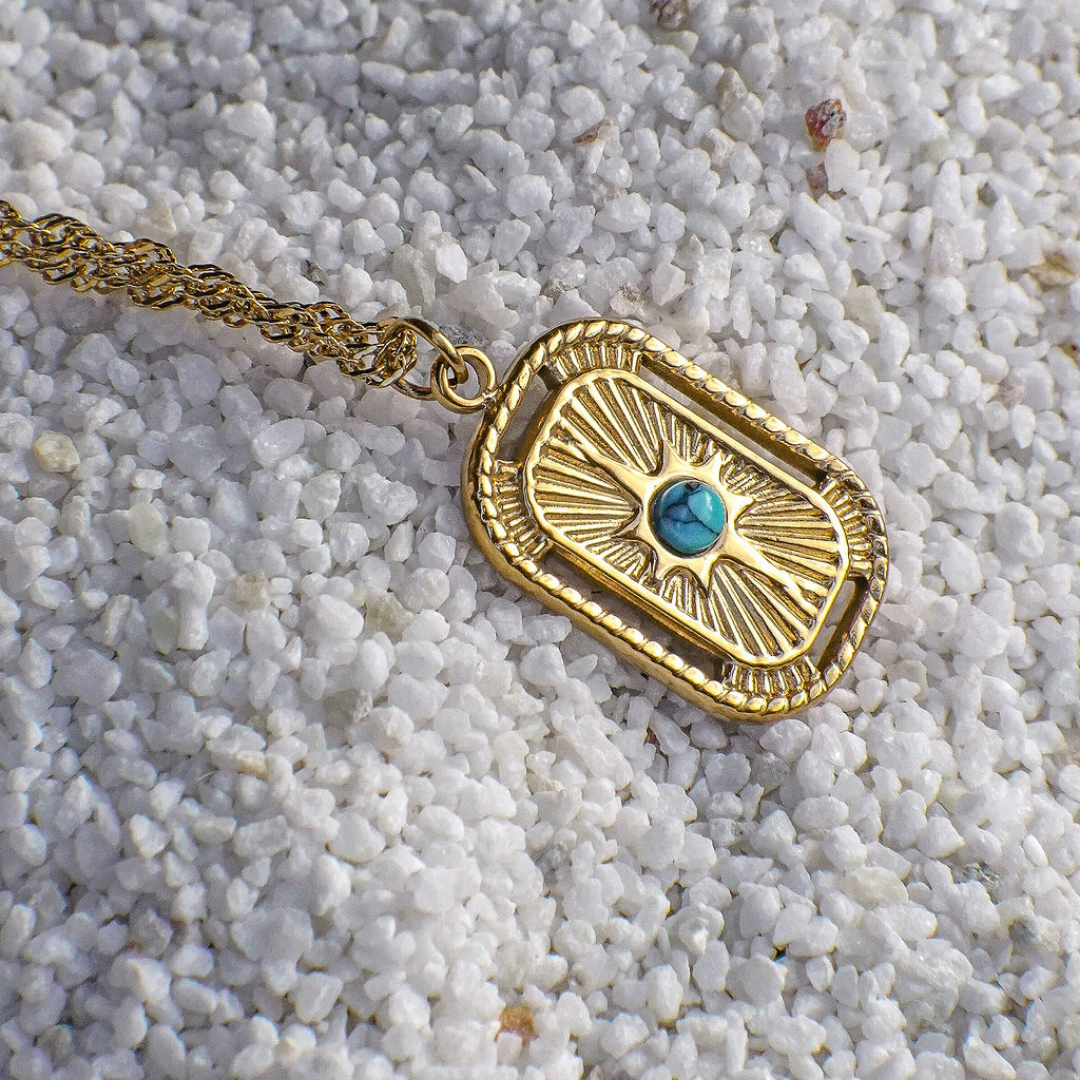 Gold necklace with a turquoise stone pendant on a sandy background