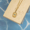 Gold necklace with a blue gemstone pendant on a beige stand against a blue background