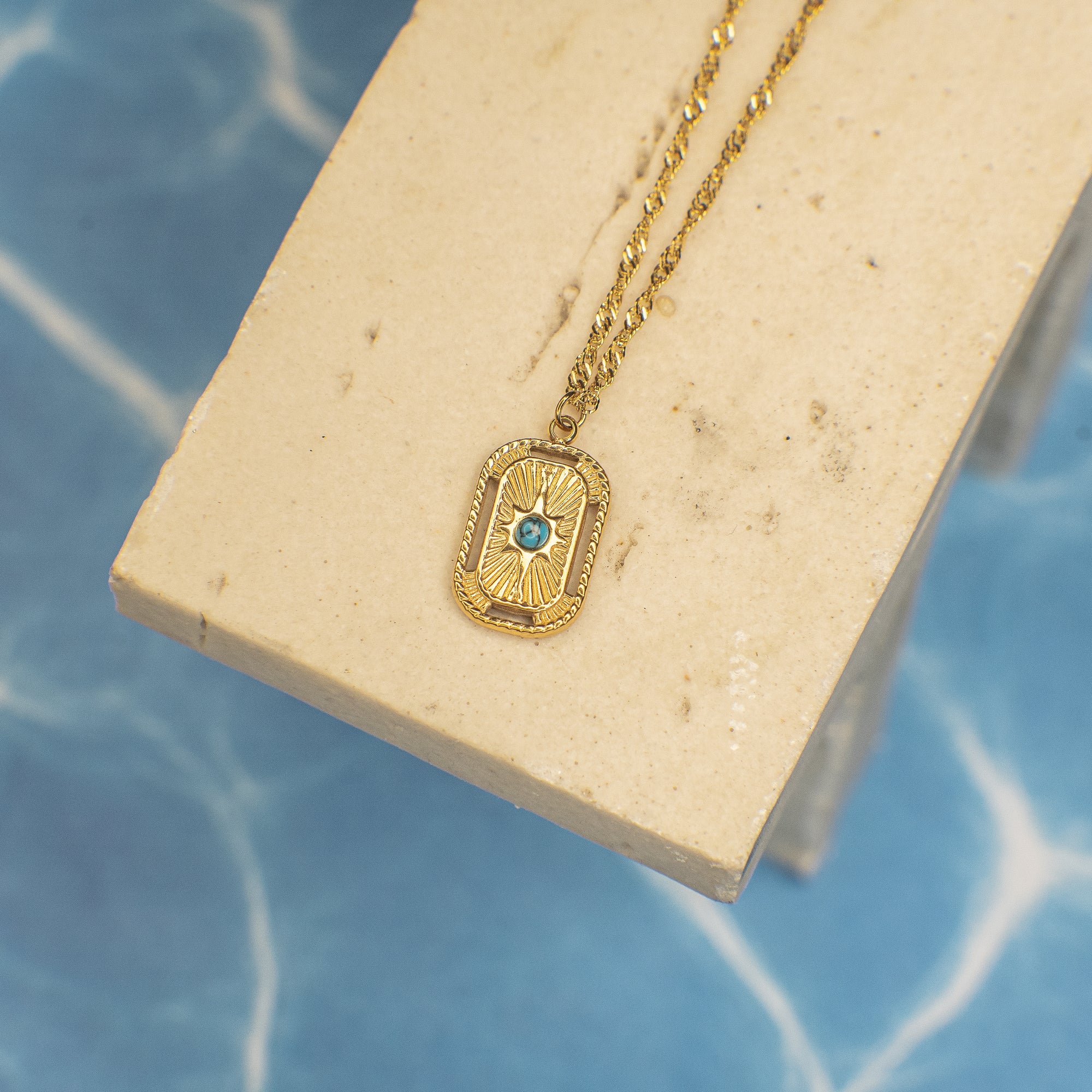 Gold necklace with a blue gemstone pendant on a beige stand against a blue background