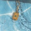 Gold necklace with a green pendant on a blue textured background