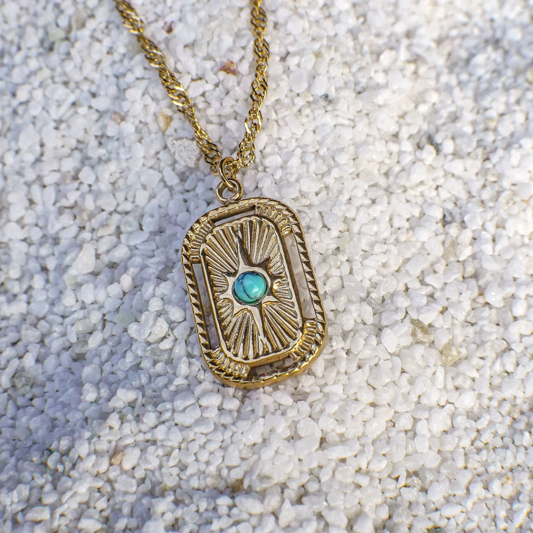 Gold necklace with a rectangular pendant featuring a blue gemstone on a textured surface.