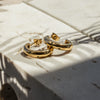 A pair of gold-colored hoop earrings with emerald star zirconia embedded on a stone surface.