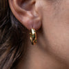 A model wearing a gold hoop earring with emerald accents made out of zirconia