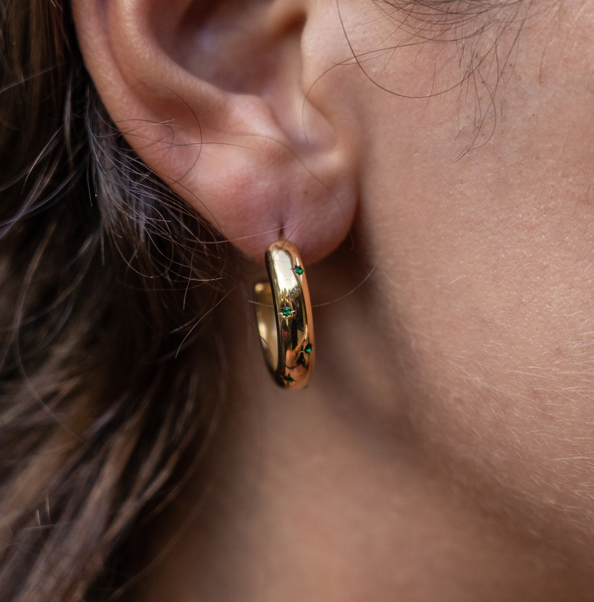 A model wearing a gold hoop earring with emerald accents made out of zirconia
