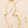 Gold necklace with leaf-like pendants on a beige stone surface