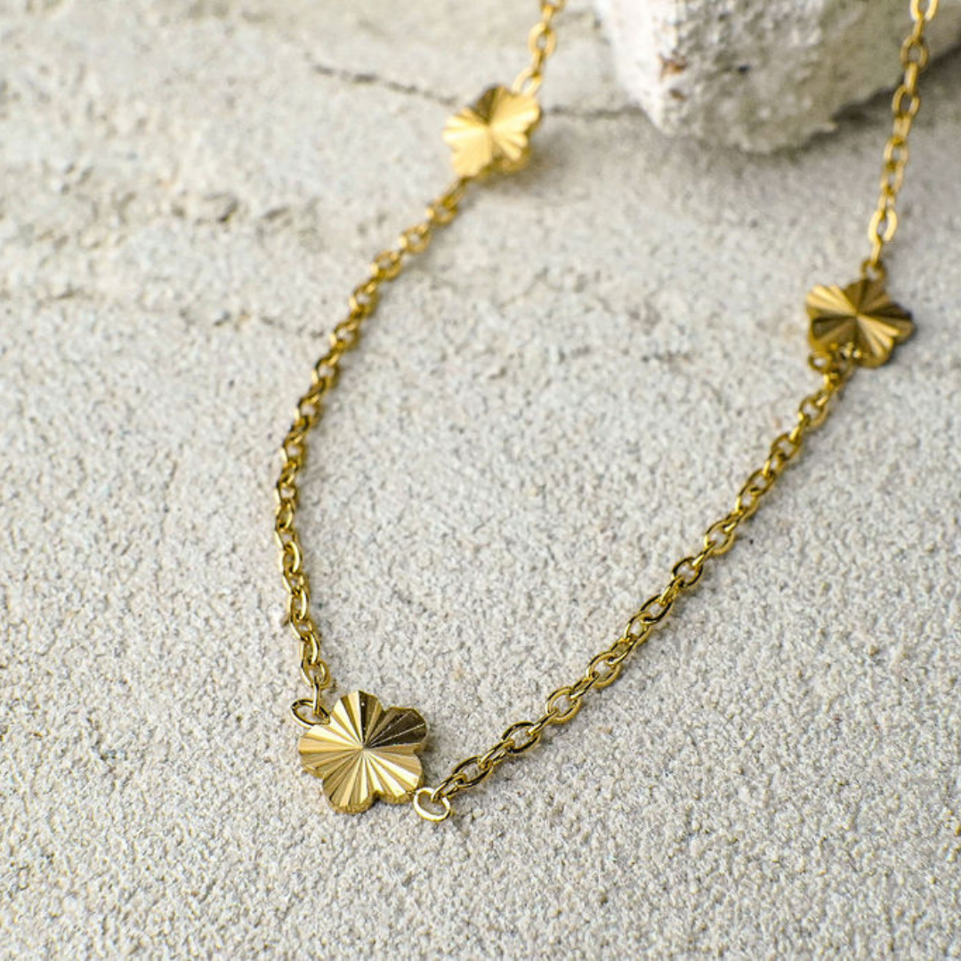 Gold necklace with leaf-shaped pendants on a textured beige surface