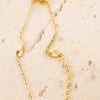 Gold necklace with leaf-like pendants on a beige stone surface