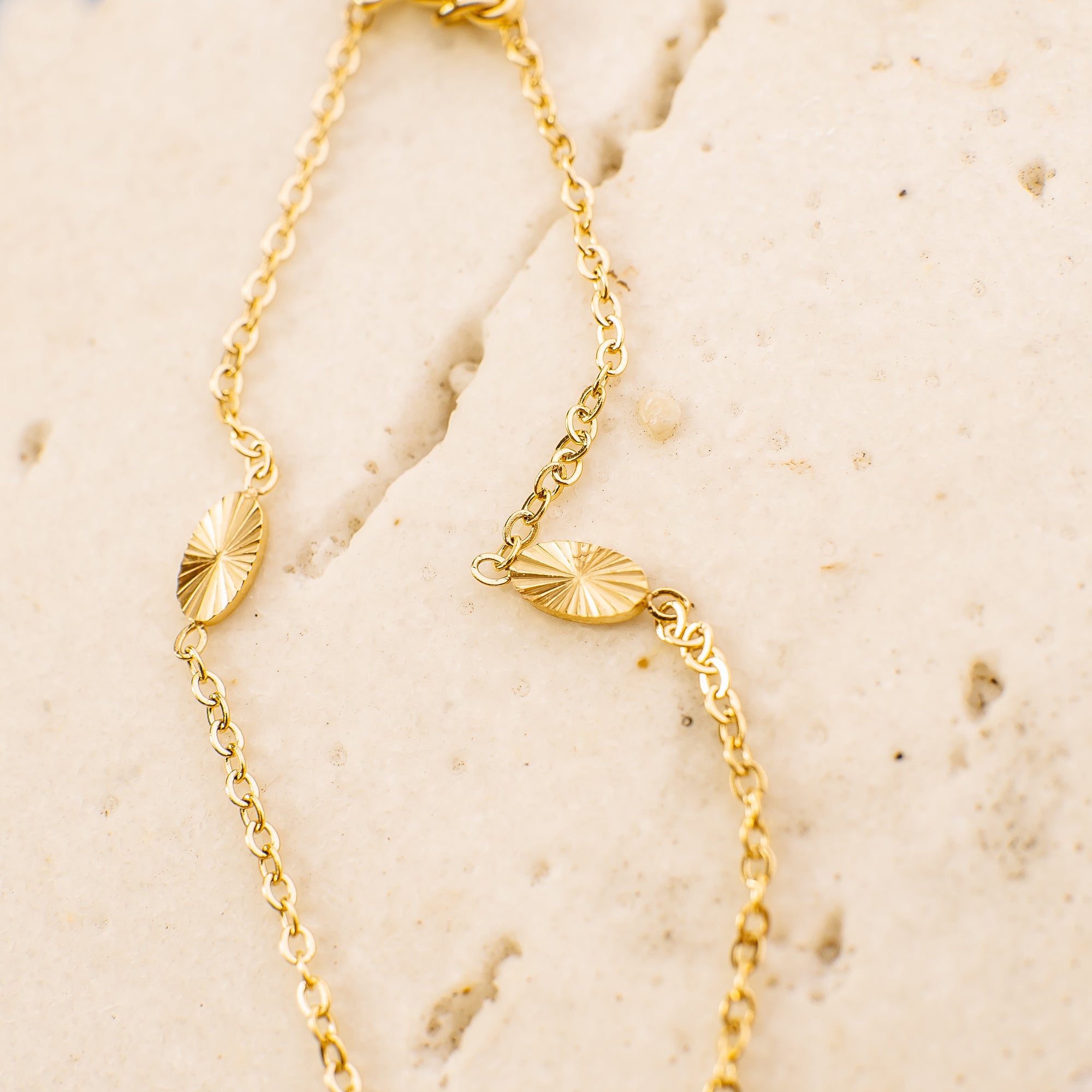 Gold necklace with leaf-like pendants on a beige stone surface