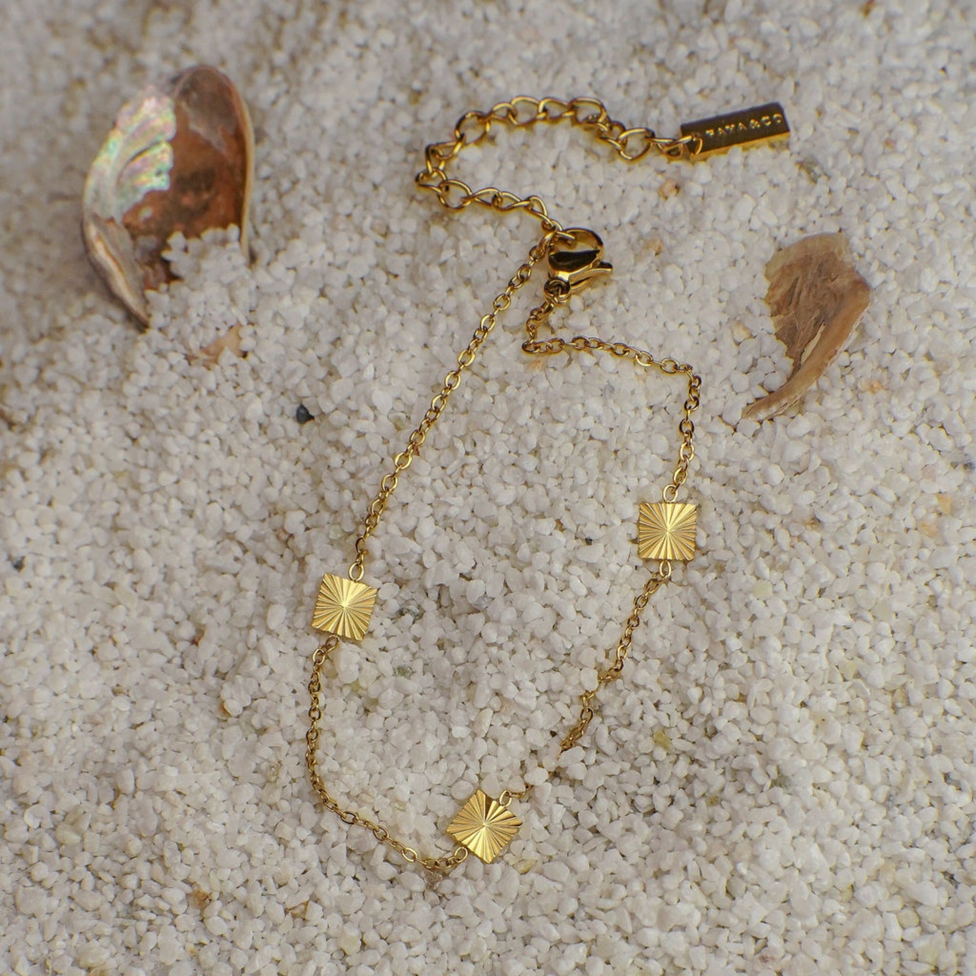 Gold bracelet with square pendants on a sandy surface