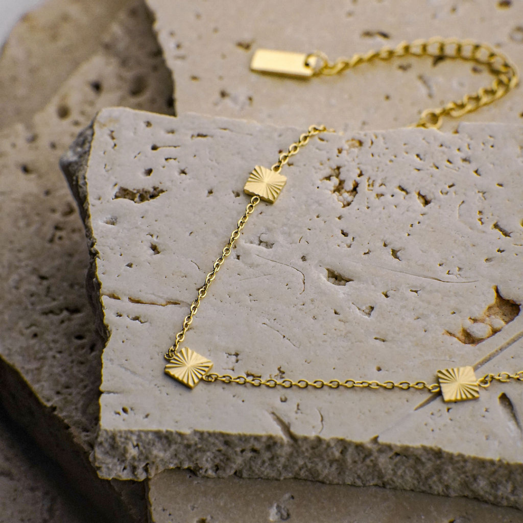 Gold bracelet with sunburst designs on a textured stone surface