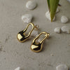 Gold earrings on a textured surface with stones and leaves